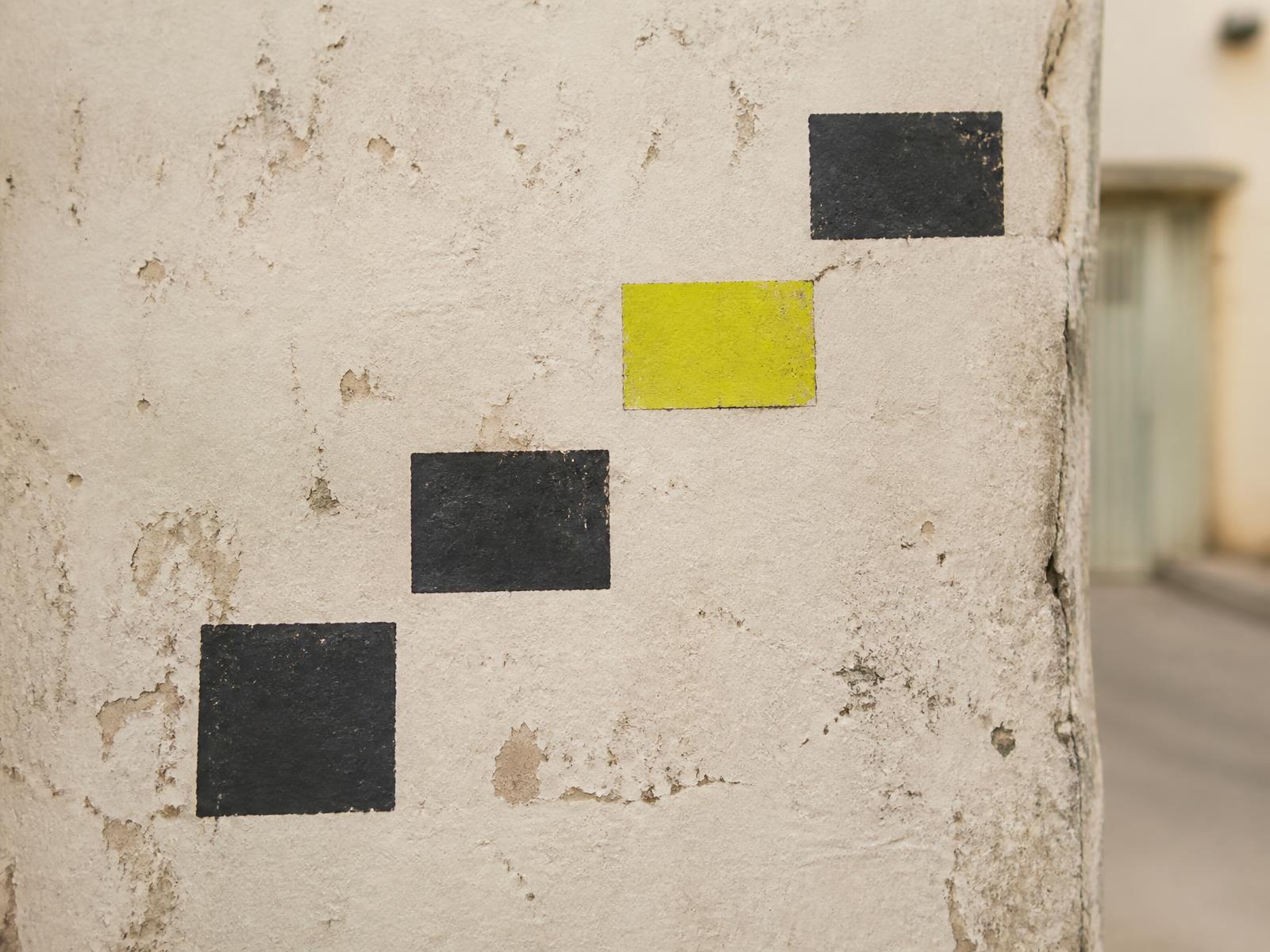 Painted blocks climbing a weathered wall, one marked in bright chartreuse